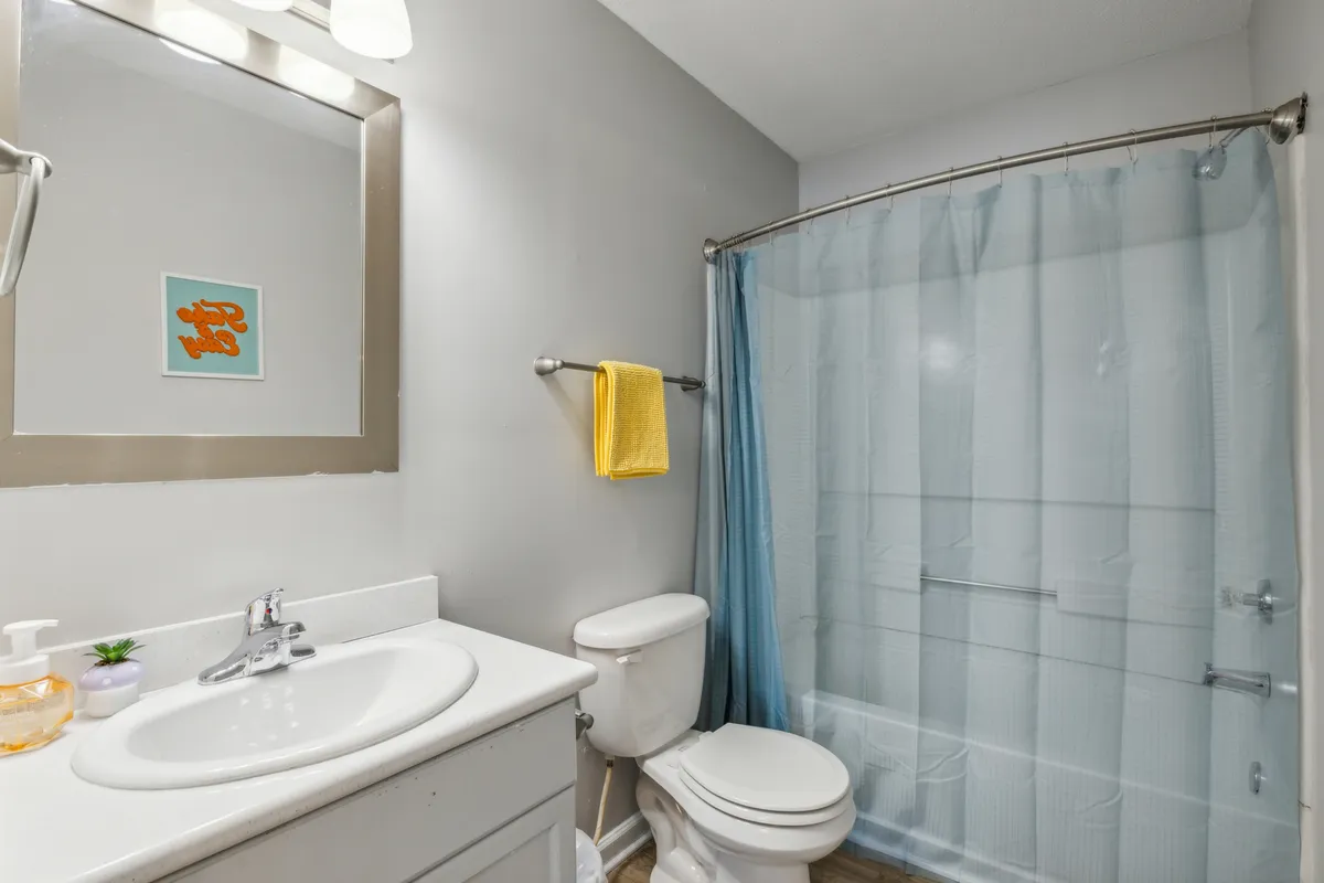 A stylish bathroom with a sink, mirror, toilet, shower curtain, colorful artwork, and a yellow towel. The space is well-lit and cheerful, supporting routines for both morning refreshment and evening relaxation.