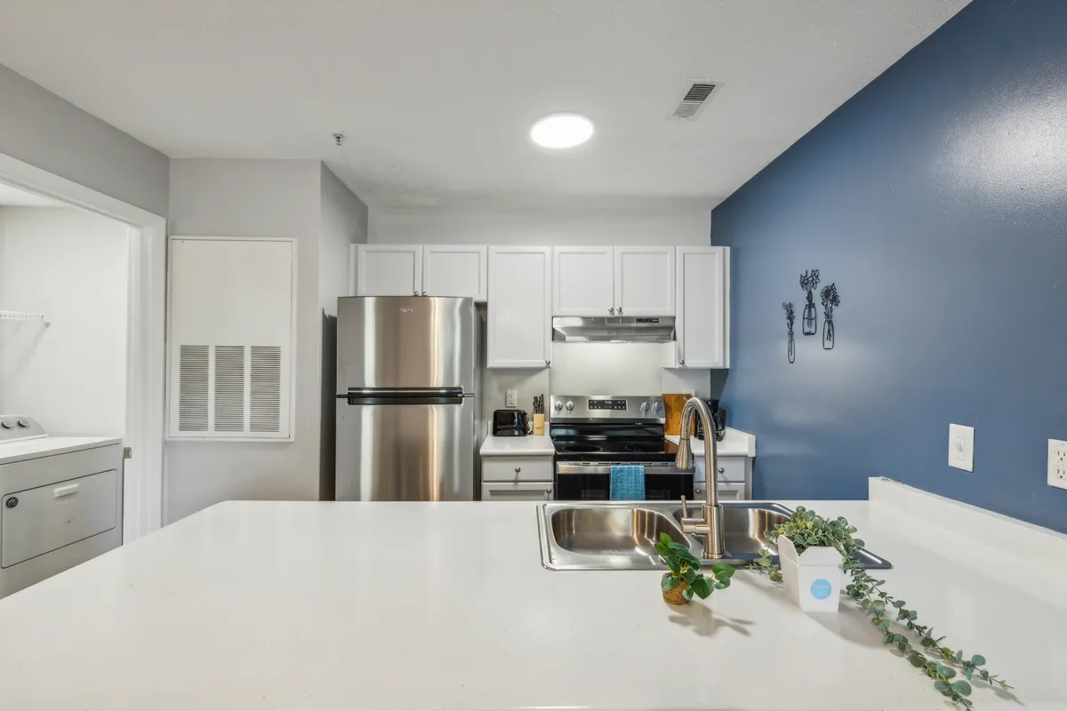 A modern kitchen featuring a spacious island, sleek stainless steel appliances, a bold blue accent wall, and a full array of kitchen utensils. The setting feels welcoming, with hints of activity such as baking cookies, hosting gatherings, or preparing weekend brunch. The scene conveys both the functionality and social potential of the kitchen.