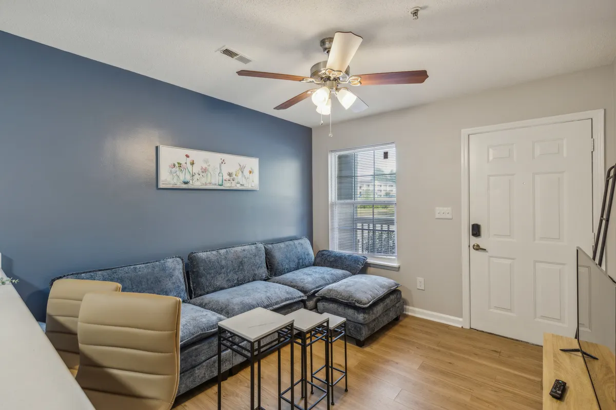 A spacious living room featuring a modern blue sectional sofa, eye-catching wall artwork, and small tables arranged for convenience. The room is bright and inviting, perfect for relaxing, socializing, or unwinding in comfort after a busy day.